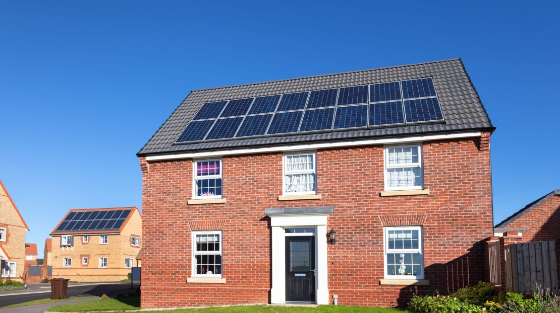 clear blue sky with a detached uk house with solar panels 